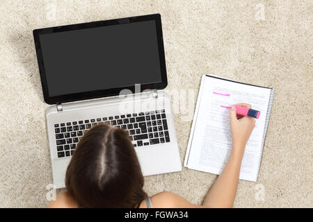 Ragazza a studiare con un computer portatile e evidenziando in un notebook sdraiato sul pavimento a casa Foto Stock