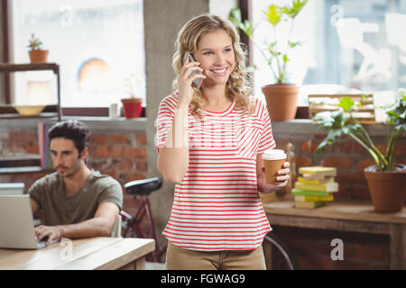 Felice imprenditrice di parlare al telefono tenendo il caffè in ufficio Foto Stock