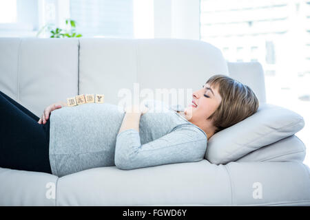 Donna incinta giocando con dei blocchi di legno mentre giaceva su un divano Foto Stock