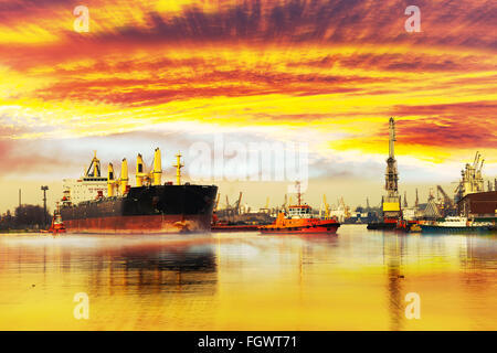 Grande nave con la scorta rimorchiatori partenza dal porto al tramonto. Foto Stock