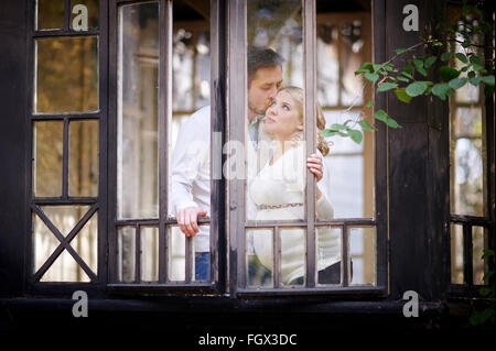 Il marito bacia la moglie incinta nella casa. Vista attraverso la finestra Foto Stock