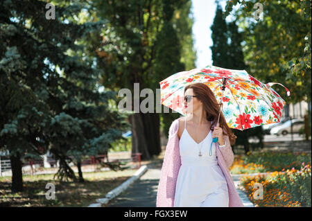 Bella donna di occhiali da sole con ombrellone a piedi nel parco Foto Stock