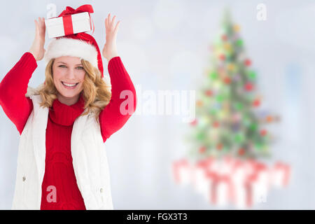 Immagine composita della donna sorridente bilanciamento regalo di Natale sulla sua testa Foto Stock