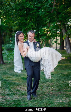 Lo sposo mantiene la sua Sposa tra le sue braccia e Sorrisi di felicità Foto Stock