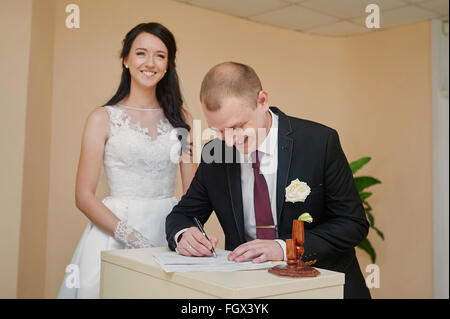 Elegante groom guardando la sua bella sposa firma registro di nozze Foto Stock