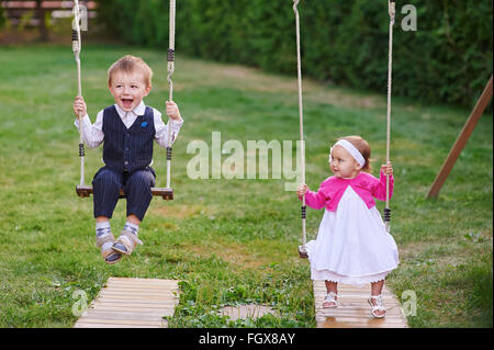 Piccolo Ragazzo e ragazza ride nel parco su uno swing Foto Stock