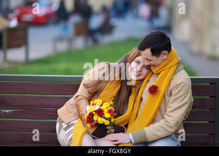 Amore giovane seduto su una panchina con un mazzo di fiori Foto Stock