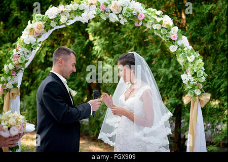 Sposa sposo abiti un anello su un dito in corrispondenza di una cerimonia di matrimonio Foto Stock