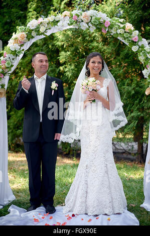Sposa e lo sposo stand vicino all'arco alla cerimonia di nozze Foto Stock