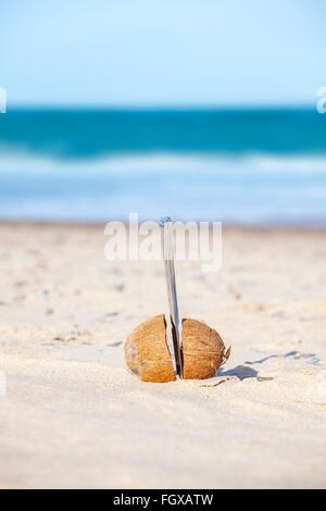 Il Cocco tagliato a metà con un coltello su una spiaggia. Foto Stock