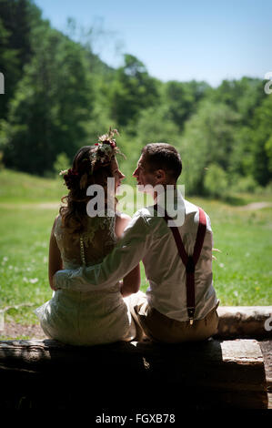 Elegante sposi sposa in abito bianco e sposo elegante seduta su una panchina nel parco Foto Stock