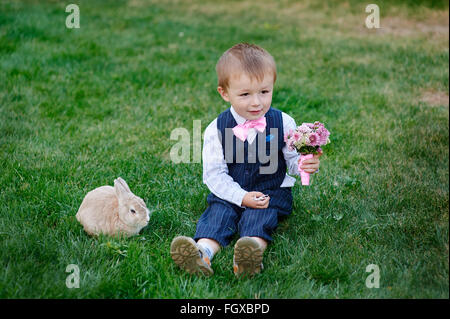 Ragazzino con un bouquet di fiori e un coniglio seduto sull'erba Foto Stock