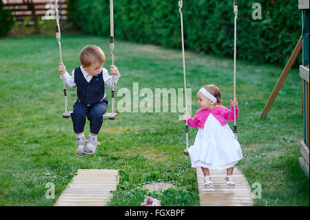 Piccolo Ragazzo e ragazza ride su uno swing presso il parco giochi nel parco Foto Stock