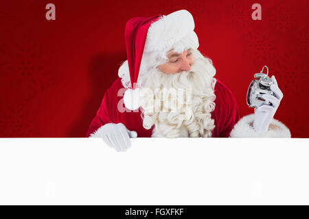 Immagine composita di felice santa tenendo sveglia e firmare Foto Stock