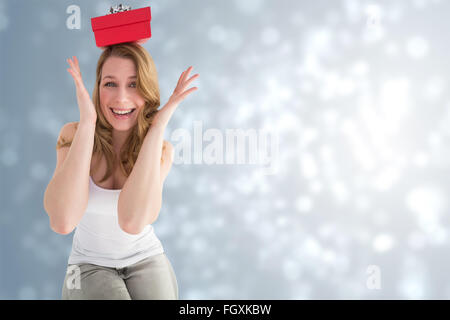 Immagine composita della donna sorridente bilanciamento regalo di Natale sulla sua testa Foto Stock