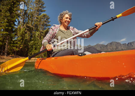 Ritratto di donna senior paddling in un lago. Felice maturo donna caucasici in canoa sul giorno di estate. Foto Stock