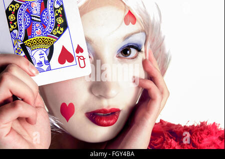 Signora giovane in possesso di una carta da gioco vicino al suo viso con la Regina di cuori sulla carta e la faccia Foto Stock