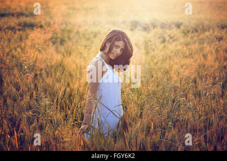 Bella giovane donna in un campo estivo. Calda luce del tramonto ritratto Foto Stock