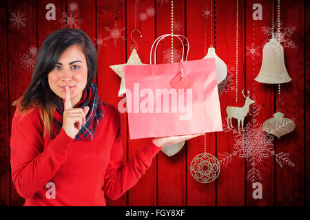 Immagine composita di brunette holding borsa regalo e mantenendo un segreto Foto Stock