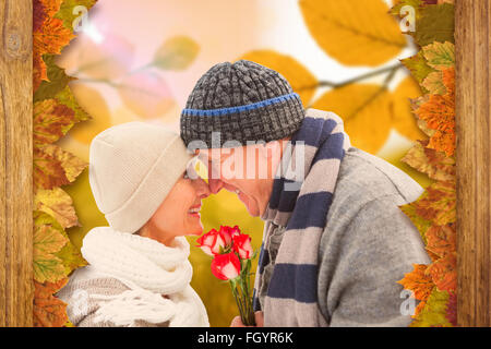 Immagine composita di felice coppia matura in abbigliamento invernale con rose Foto Stock