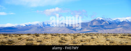 Strada sterrata vagare attraverso il deserto per un Snow capped montuosa sotto il cielo blu con nuvole. Foto Stock