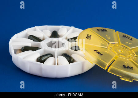 Giallo e Bianco rotondo pillola settimanale caso sullo sfondo blu Foto Stock