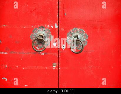 Vecchia porta rossa con bronzo doorknockers che mostrano il cinese taoista di simboli Foto Stock