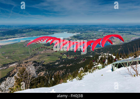 Füssen, Germania - 09 Aprile 2015: rosso start di parapendio da Tegelberg oltre l'Foggenlake Seq Foto Stock