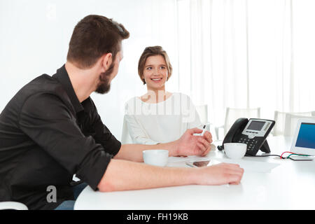 Due giovani sorridenti business persone sedute e parlare sulla riunione in ufficio Foto Stock