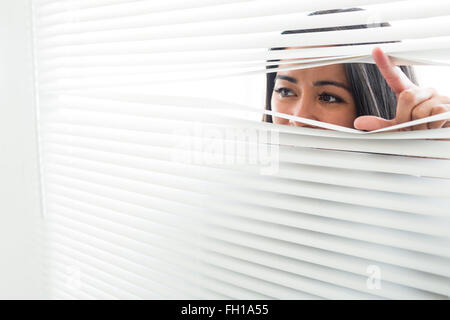 Donna spiata attraverso alcuni ciechi della finestra Foto Stock