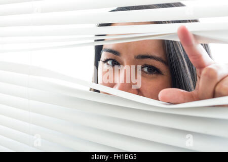 Donna spiata attraverso alcuni ciechi della finestra Foto Stock