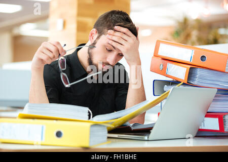 Imprenditore triste seduta al tavolo con molte cartelle in ufficio Foto Stock