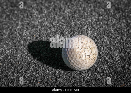 Il crack pallina da golf con la luce del sole ed ombra messo sul putting green in nessun colore. Foto Stock