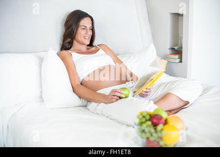 Donna felice la lettura di romanzo con la Granny Smith sul letto Foto Stock