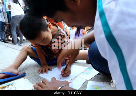 La dinamica società Teen (DTC) volontari mentre l'insegnamento di un giovane ragazzo come scrivere il suo nome durante la Kariton Klasrum (Pushcart Classroom) condotta in Brgy. 5, Alonzo Street, Dalahikan, Cavite City. I fondatori di DTC trovano compimento che lentamente a crescere il numero di giovani che viene trasformato attraverso i loro programmi. Trasformate la gioventù, che hanno usato per essere tossicodipendenti, petty ladri, decontaminanti, bambini di strada, drop-out e out-of-scuola sono ora il DTC volontari e hanno restituito al sistema di istruzione tradizionale. Mentre alcuni dei bambini rimangono al di fuori della scuola che, almeno, sono in grado di accedere a basic educa Foto Stock