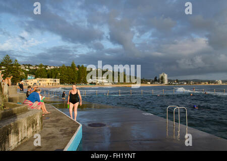 Persone sedute e in piedi accanto ad una piscina oceanica presso la spiaggia di Collaroy di Sydney al mattino presto in Australia Foto Stock