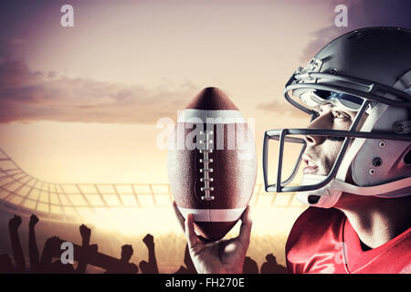 Immagine composita di sportivo guardando verso l'alto tenendo premuto il football americano Foto Stock