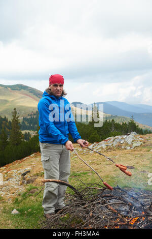 Escursionismo uomo preparare gustose salsicce sul fuoco Foto Stock