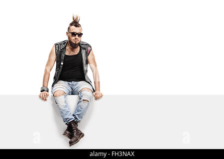 Giovani punk rocker con un Mohawk acconciatura e un giubbotto in pelle seduta su un pannello isolato su sfondo bianco Foto Stock