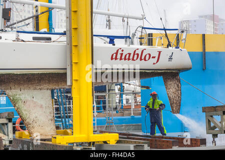 Un tecnico di manutenzione con una rondella di pressione pulisce la chiglia e la parte inferiore di uno yacht Foto Stock