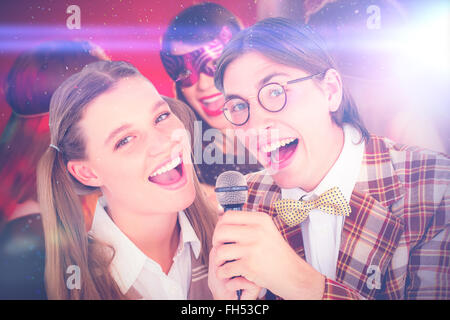 Immagine composita di felice geeky hipsters cantando con microfono Foto Stock