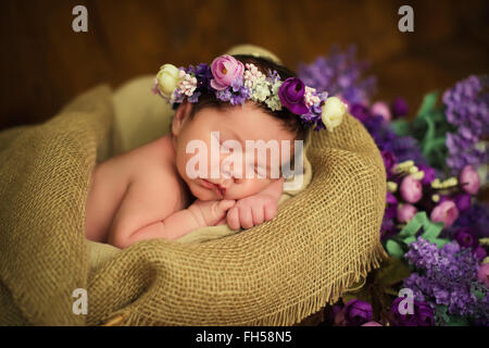 Bella neonato ragazza con una corona di fiori viola dorme in un cesto di vimini Foto Stock