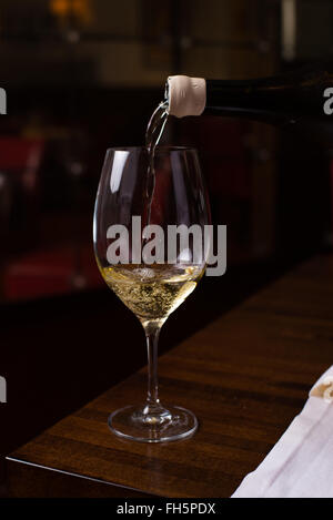 Un azione girato di vino bianco che viene versato in un bicchiere in un buio ristorante l'impostazione. Foto Stock