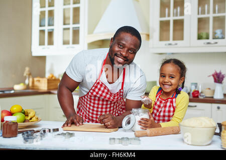 Uomo allegro e simpatico bambina in grembiuli andando a cuocere la pasticceria Foto Stock