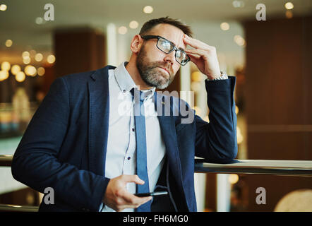 Malinconici dipendente con il cellulare appoggiato sulle ringhiere nel centro business Foto Stock