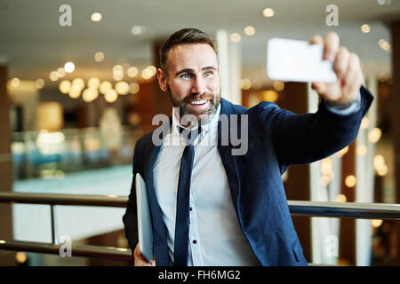 Happy businessman con gadget rendendo la sua selfie in ambienti interni Foto Stock