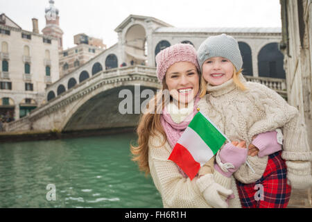 Famiglia moderna prendendo una pausa invernale per godere di avventura ispirato a Venezia, Italia. Felice madre e figlia holding bandiera italiana mentre in piedi di fronte a Ponte di Rialto Foto Stock