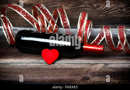 Rosso Cuore di legno, bottiglia di vino rosso e bellissimo nastro sul vecchio di tavole di legno. Composizione romantica. Foto Stock