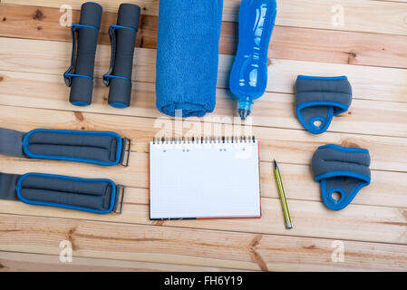 Attrezzature sportive. Manubri, caviglia, pesi pesi da polso, asciugamano, Bevanda isotonica e Notebook al piano di allenamento su schede. Foto Stock