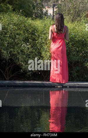 Donna in abito rosso in piedi presso la piscina Foto Stock